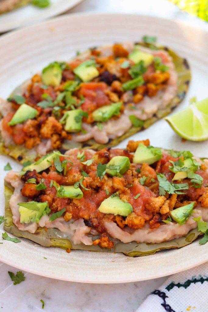 huaraches de nopal on a beige plate with avocado and salsa on top.