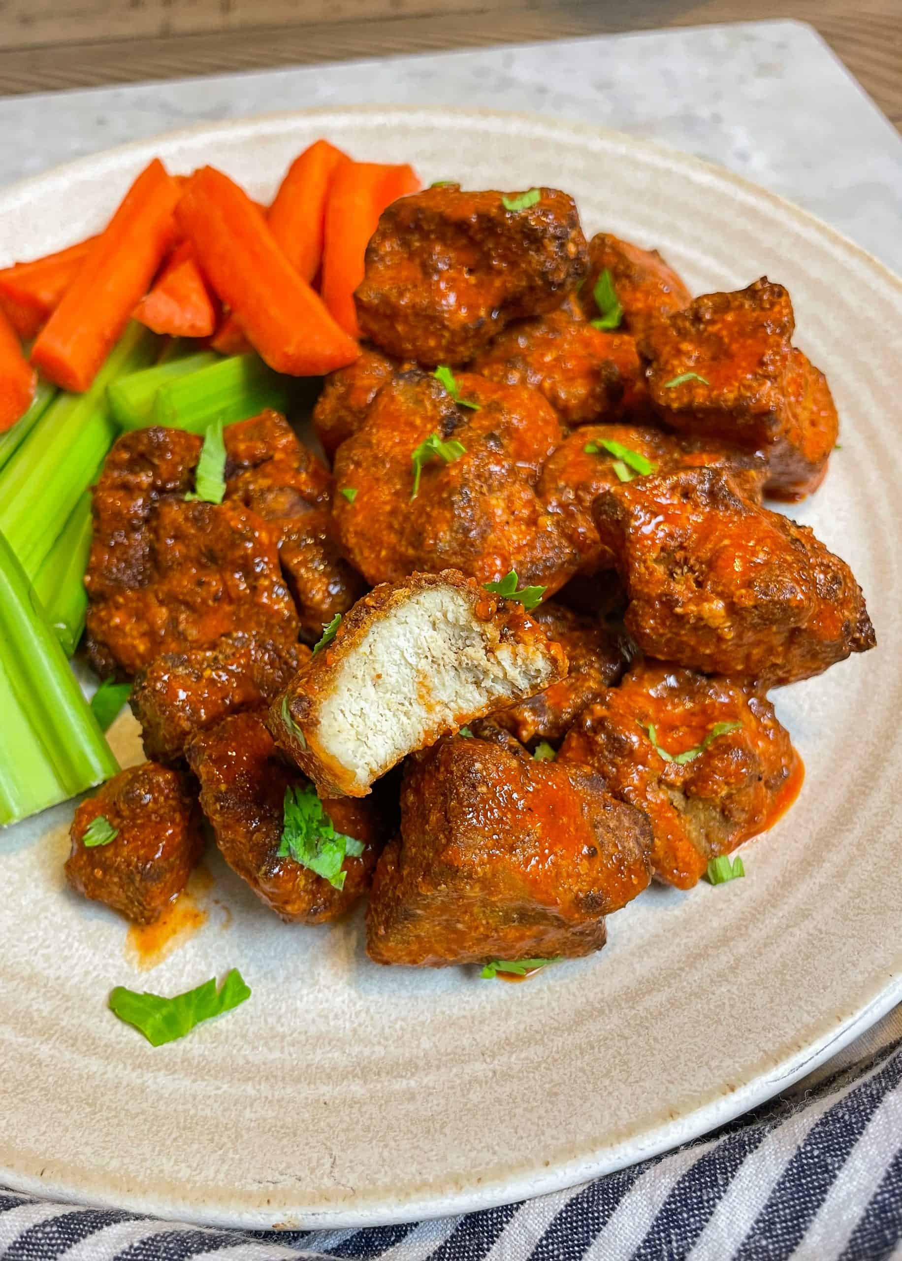 buffalo tofu wings on a beige plate with celery and carrots.